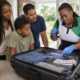 Black Caribbean pest-control technician showing a South Florida family how to inspect suitcase seams after holiday travel